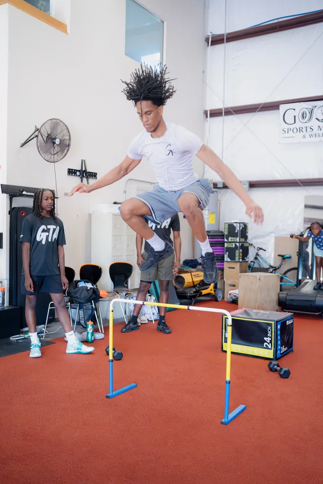 Athlete in mid-air over a hurdle with teammates watching