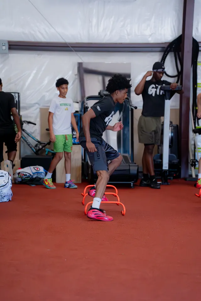 Athletes stepping through a mini-hurdle line while a coach watches